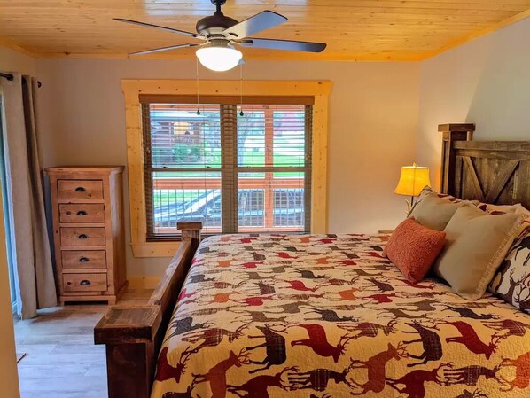 A bedroom with a bed, a wooden dresser, a window with blinds, a ceiling fan, and a lamp. - Easy access! Mountain Views,Watch the Elk, Fire Pit,Close to Skiing,Tubing, Golf (Maggie Valley)