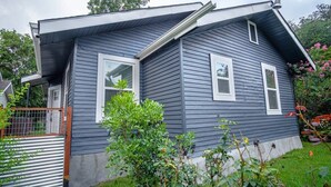 Una casa de dos pisos con revestimiento exterior oscuro, molduras blancas alrededor de ventanas y puertas, y un techo inclinado.