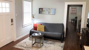 Una sala de estar con un sofá gris, una mesita auxiliar y una obra de arte colgada en la pared.