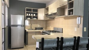 Cocina compacta con refrigerador, estufa y mesa de comedor con sillas.
