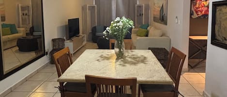 A dining area with a table and chairs, a hanging light fixture, and a vase with flowers.
