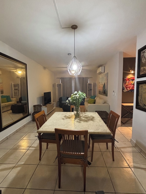 A dining area with a table and chairs, a hanging light fixture, and a vase with flowers.