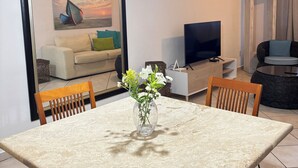 Comedor con mesa, sillas, un jarrón con flores, televisor y una lámpara colgante moderna.