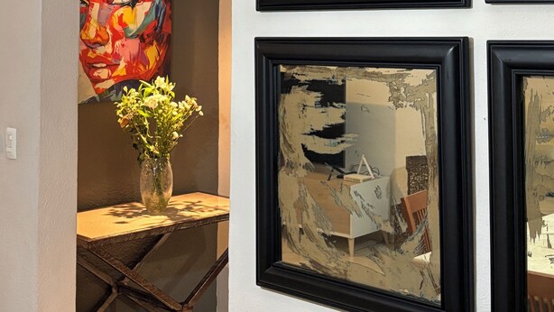 Una habitación con pared blanca, un cuadro abstracto con marco negro, un jarrón con flores y una mesa con diseño geométrico.