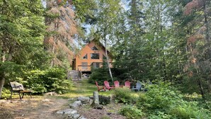 Eine Hütte, umgeben von einem Wald, mit einem Pfad, der dorthin führt, und mehreren Adirondack-Stühlen in der Nähe des Eingangs.