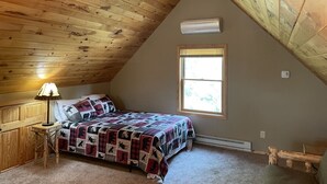 Ein Schlafzimmer mit schrägverdachter Decke, einem Bett mit gemustertem Quilt, einem Fenster und einem Deckenventilator.