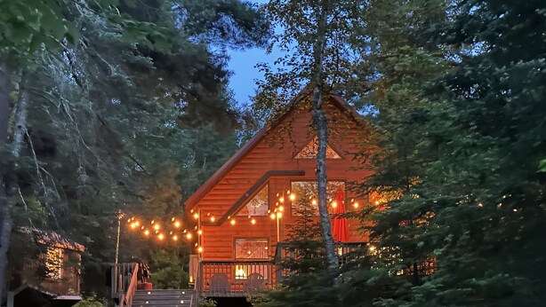 Eine Holzhütte mit Veranda, umgeben von Bäumen und einer Holztreppe, die zu ihr hinaufführt.