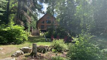 Une cabane entourée d’une forêt dense, dotée d’une terrasse en bois et d’un espace salon extérieur.