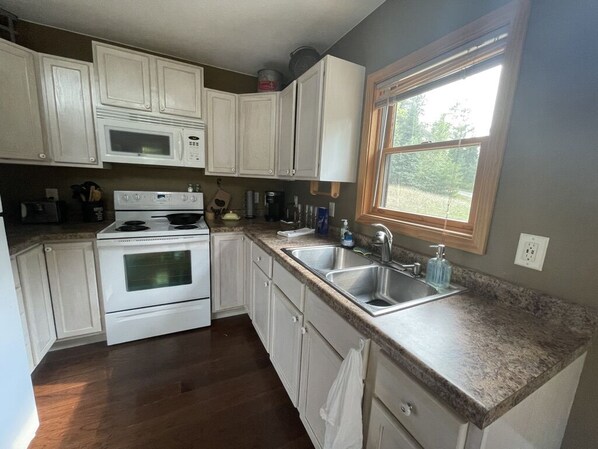 A kitchen with white cabinets, a stove, a microwave, a sink, and a window.