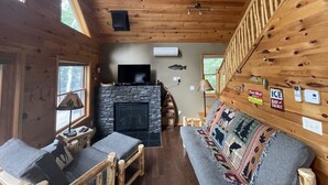 Ein Blockhaus-Interieur mit Kamin, Holzwänden, einer Couch und einem Fernseher.