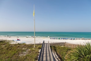 A beach with a wooden boardwalk leading to the water, a flagpole, and beach umbrellas.