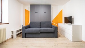 Una habitación moderna con un sofá gris, un tocador blanco y un televisor sobre un mueble.