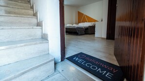 Una escalera conduce a una habitación con una cama, un sofá y piso de madera. Se observa un felpudo con la inscripción "Italianway".