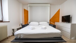 Una habitación de hotel moderna con cama, televisor, cómoda y ventana con cortinas.