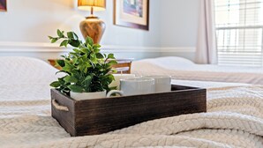 A wooden tray with a potted plant and white mugs on a bed with a white textured blanket.
