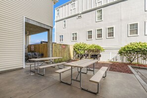 Een terras buiten met picknicktafels en uitzicht op een gebouw met meerdere ramen.