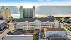 A multi-story hotel with balconies, a swimming pool, and a view of the ocean.