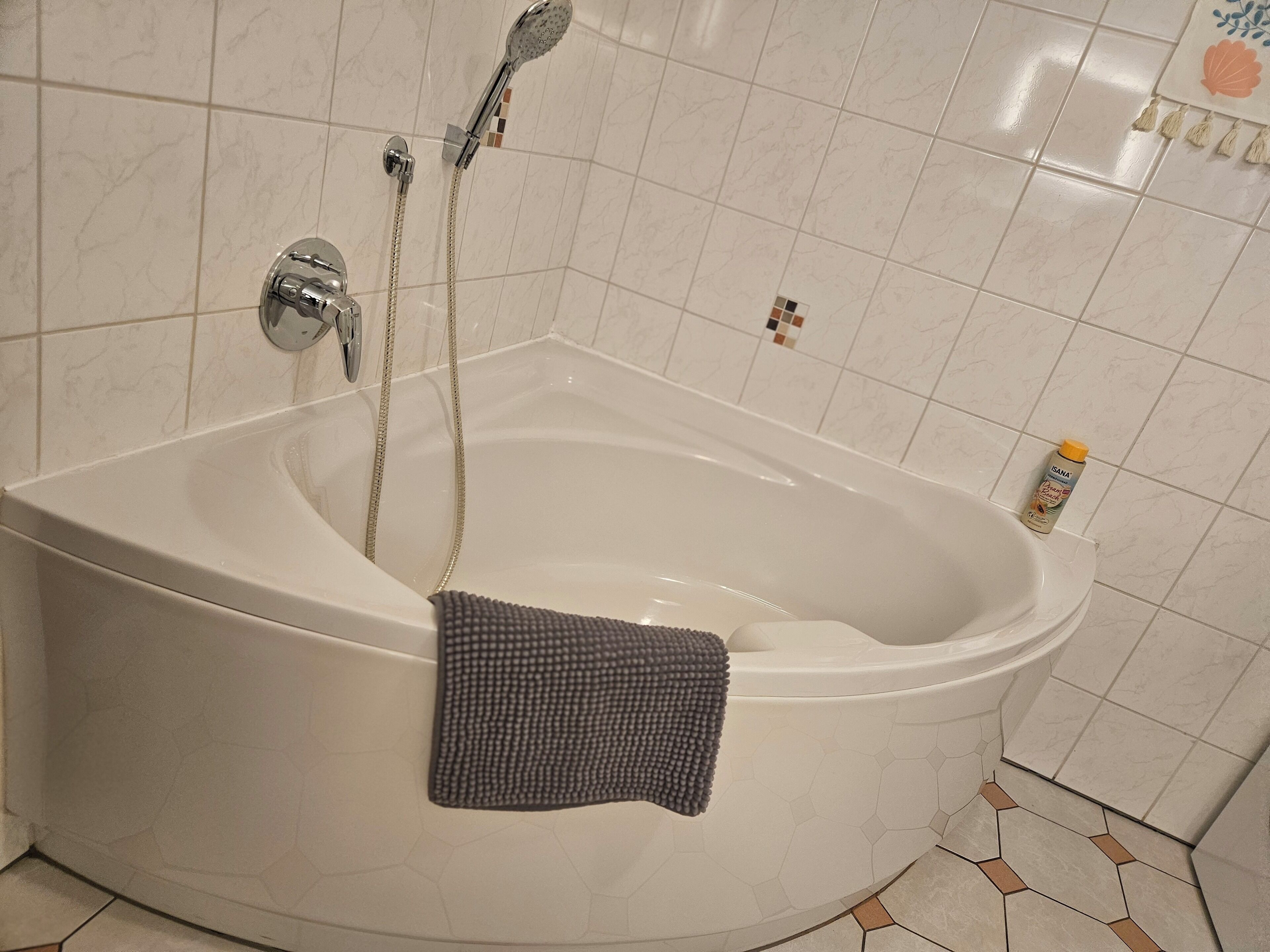 A bathtub with a shower head and hose, a towel, and a bottle of lotion on the side.