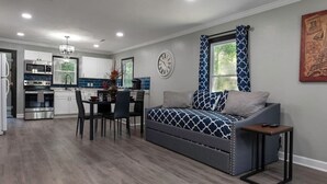 Een moderne keuken met inbouwapparatuur, een zithoek met tafel en stoelen, en een bank met gestreepte kussens.