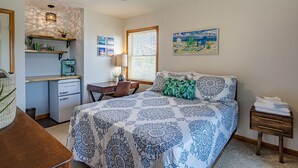 A bedroom with a bed, a desk, a chair, a small table, a nightstand, a ceiling fan, and a window with blinds.