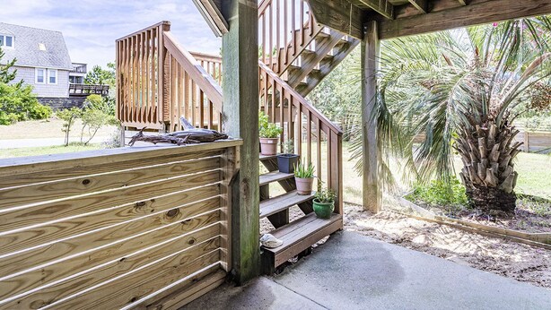 A wooden deck with a staircase leading to a covered area, surrounded by potted plants and a palm tree.