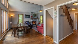 A spacious living area with a fireplace, wooden flooring, a dining table with chairs, a red sofa, and a staircase. - Aspen View - 3-story home with gorgeous views, a hot tub, and perfect location! (Blowing Rock)