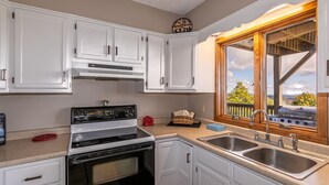 A kitchen with white cabinets, a stove, a sink, and a window with a view of trees and mountains. - Aspen View - 3-story home with gorgeous views, a hot tub, and perfect location! (Blowing Rock)