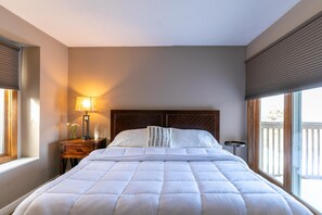 Un letto rifatto con cura, una testiera, una lampada da comodino e un comodino con un vaso di fiori.