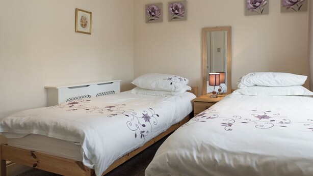 A bedroom with two beds, a nightstand, a lamp, and floral wall art. - 3 bedroom accommodation in Windermere (Windermere)