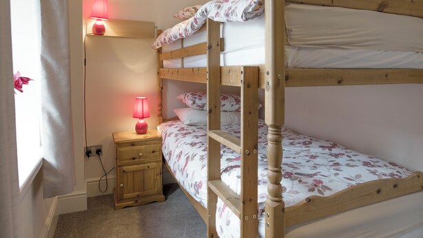 A bunk bed room with a bedside table, a lamp, and a window with curtains.
