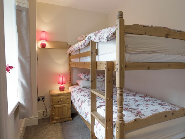 Une chambre avec un lit superposé, une table de chevet, une lampe et une fenêtre avec des rideaux.