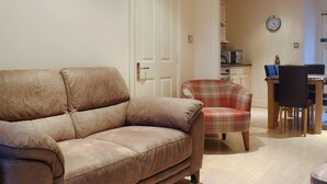 A living room with a beige sofa, a plaid armchair, and a dining area with a table and chairs. - 3 bedroom accommodation in Windermere (Windermere)