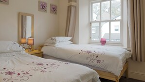 A bedroom with two beds, a window with curtains, a bedside table with a lamp, and wall art.