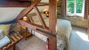 Une chambre mansardée chaleureuse, avec un plafond en pente, une échelle en bois, un lit avec une literie à motifs, une table de chevet avec une lampe et une fenêtre avec des rideaux.
