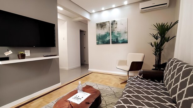Uma sala de estar moderna com televisão de tela plana, sofá, mesa de centro e uma poltrona.
