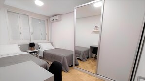 Quarto com duas camas, um guarda-roupa, uma escrivaninha e um espelho.