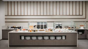 Un bar à petit-déjeuner moderne proposant une variété d’aliments et de boissons, notamment des machines à café, ainsi qu’un assortiment de fruits et de viennoiseries.