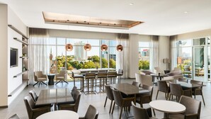 A modern hotel dining area with multiple tables and chairs, large windows offering city views, and a contemporary ceiling design. - AC Hotel by Marriott Raleigh Downtown (Raleigh)