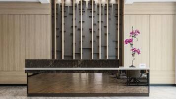 A reception desk with a dark marble top, a light wood panel wall, and a single pink orchid in a vase.