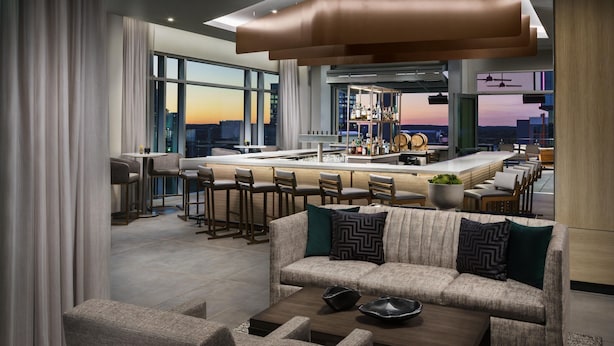 A modern living room with a sofa, coffee table, and bar area with stools. - AC Hotel by Marriott Raleigh Downtown (Raleigh)