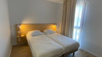 A double bed with a wooden headboard, two bedside tables, and a window with curtains.