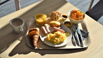 Bandeja de desayuno con cruasanes, salchichas, huevos revueltos y un tazón de albaricoques sobre una mesa de madera.
