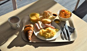 Bandeja de desayuno con cruasanes, salchichas, huevos revueltos y un tazón de albaricoques sobre una mesa de madera.