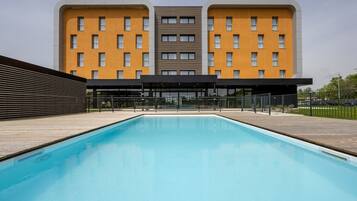 Un hotel moderno con piscina, un espacio exterior cubierto y un edificio de dos plantas con una fachada amarilla distintiva.