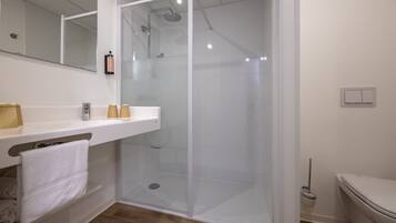 A bathroom with a glass-enclosed shower, a white sink with a mirror, and a toilet.