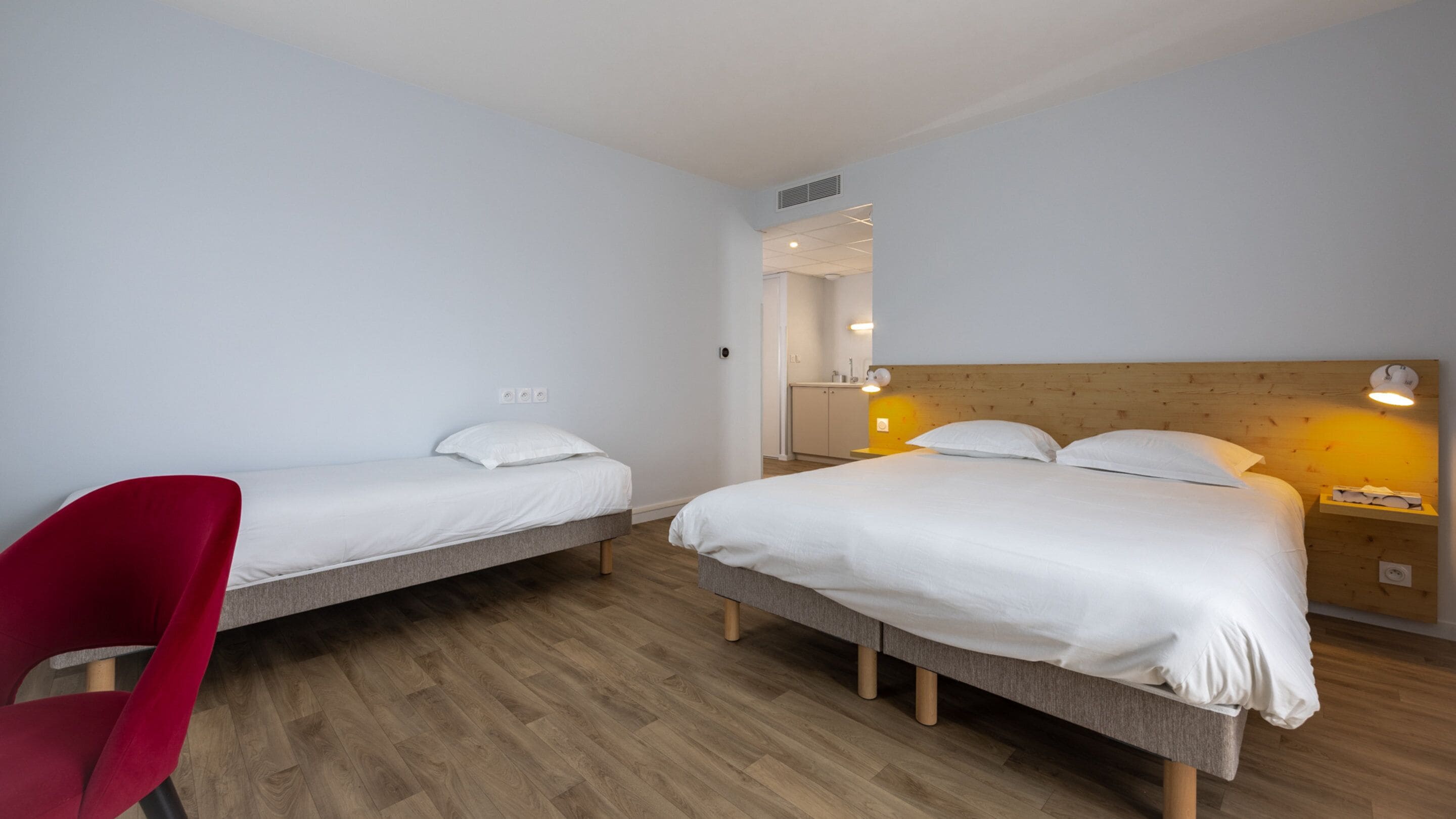 Hotellihuone, jossa on kaksi erillistä sänkyä, punainen tuoli ja puinen pääty.