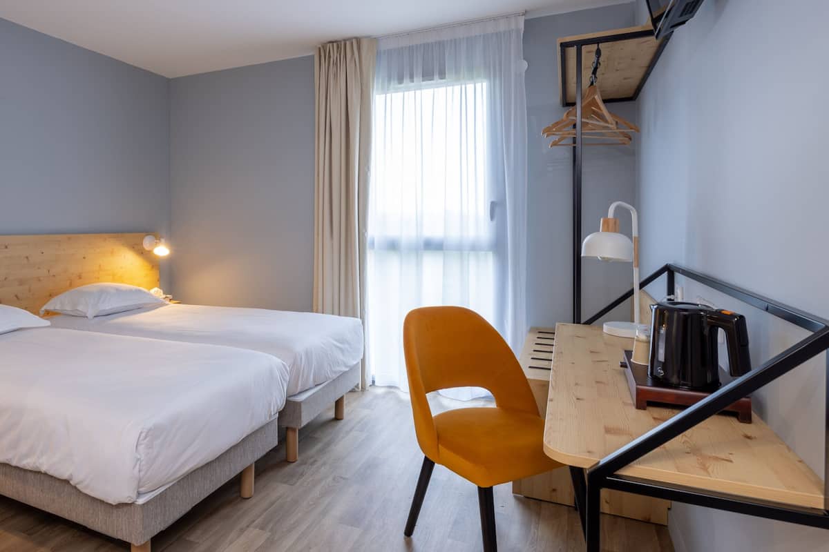 A hotel room with two beds, a desk with a chair, a coffee maker, and a hanging coat rack.