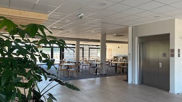 A spacious indoor area with multiple tables and chairs, a large potted plant, and a door with an elevator.