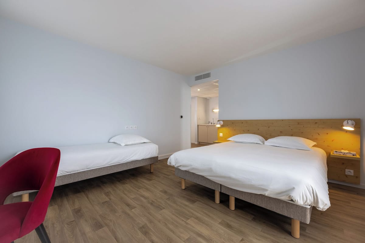 A hotel room with two single beds, a red chair, and a wooden headboard.