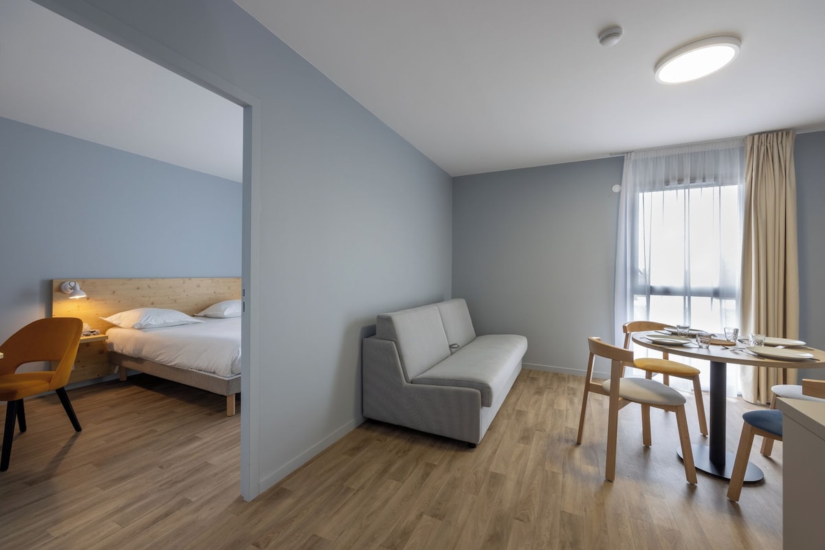 A modern, well-lit room with a bed, sofa, dining table, and chairs.